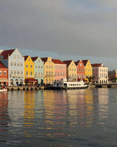 Colorful pastel Handelskade waterfront buildings reflected in Willemstad harbor at golden hour in Curaçao